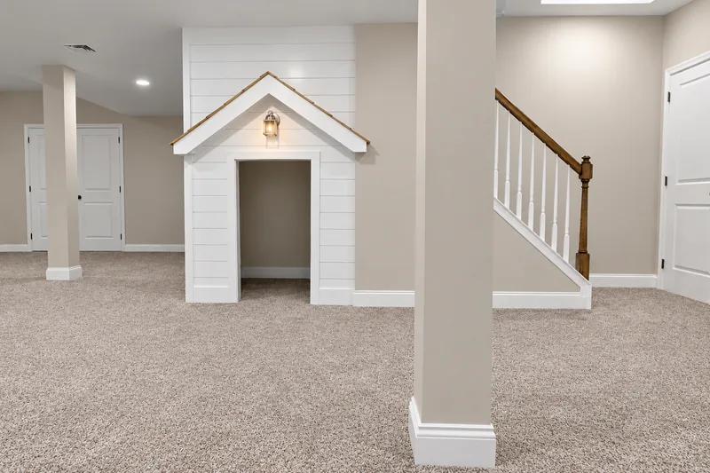 Carpeted basement with a small playhouse beneath the stairs